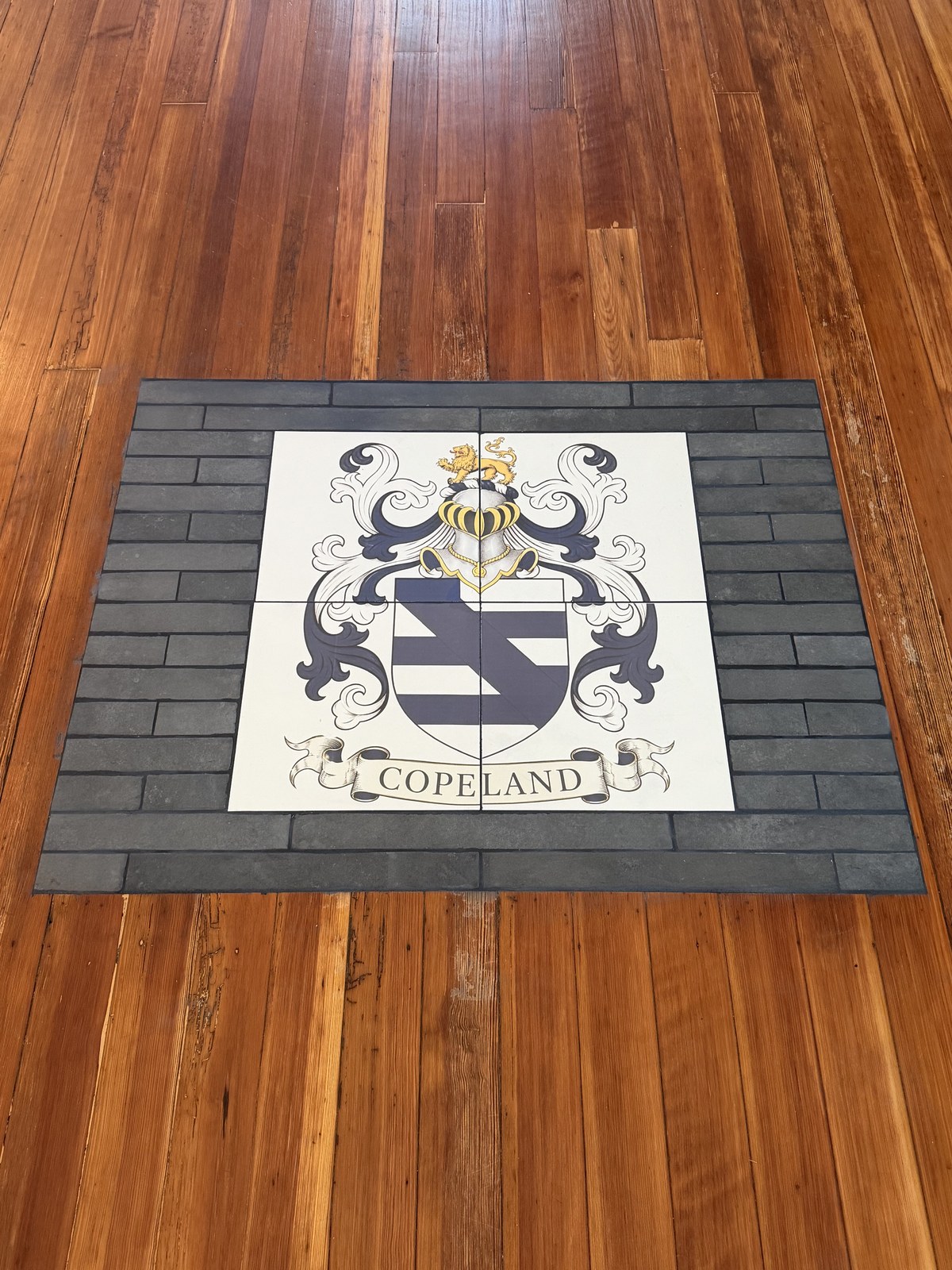 Close-up of the Copeland coat of arms and family name across four custom printed floor tiles with a dark tile border.