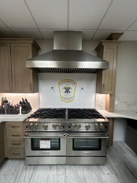 Eastchester EMS Commercial Kitchen Backsplash — Front View Front view of the Eastchester EMS logo tile backsplash above the stainless-steel range in the station kitchen.