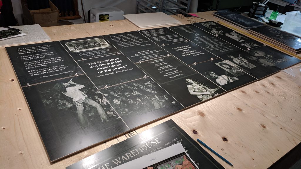 Black-and-white concert photographs and quotations printed across The Warehouse outdoor tile mural, laid out with spacers on the workshop table.
