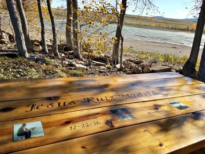 Outdoor Memorial Photo Tiles in a Lakeside Picnic Table Three memorial photo tiles embedded in a wooden picnic table beside a lake, surrounded by autumn trees.